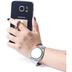 A hand holding a black Samsung phone equipped with a metallic holder, wearing a silver watch. The image features a logo.