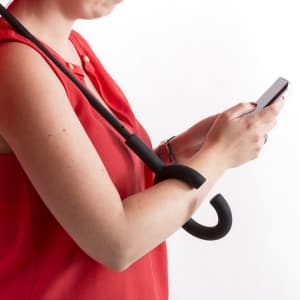 A reversible umbrella in black, held by a person while using a smartphone. The umbrella features a hook handle.