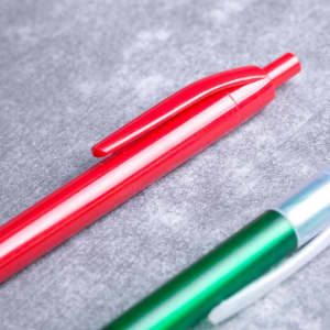 A red plastic pen with a clip, positioned above a green plastic pen, both set against a grey background.