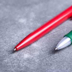 Two plastic pens, one red and one green, with a silver detailing on the green pen, resting on a grey surface.