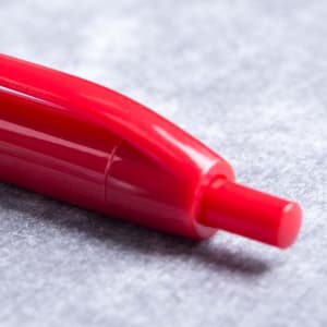A red plastic pen with a smooth finish and a rounded tip, resting on a grey surface.