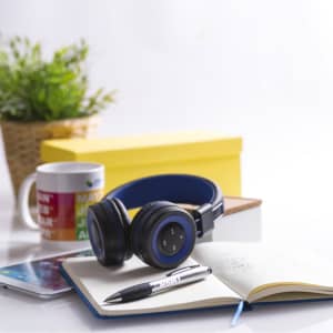 A pair of blue Tresor headphones rests on a notebook, with a pen and a smartphone nearby, alongside a plant and a mug.