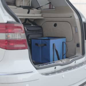 A blue organiser bag with black handles sits in the boot of a car, alongside other bags.
