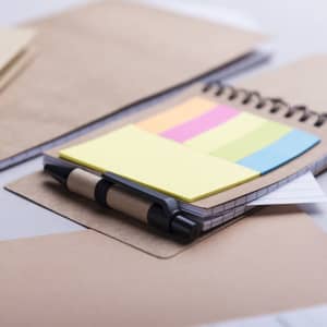 A sticky notepad featuring yellow, pink, and blue notes, placed on a brown folder with a pen beside it.