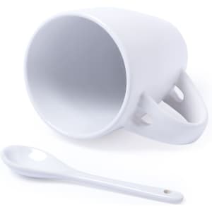 A white ceramic mug with a unique handle design and a small matching spoon beside it.