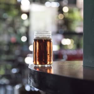 A drink bottle in a glass jar filled with amber liquid, sitting on a wooden surface with a blurred background.