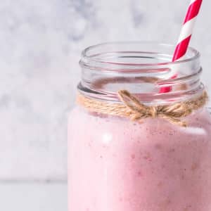 A drink bottle made of glass with a rustic twine wrap, filled with pink smoothie and a red-and-white striped straw.