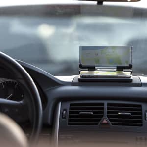 A car phone holder with a transparent screen, positioned on the dashboard, displaying navigation.