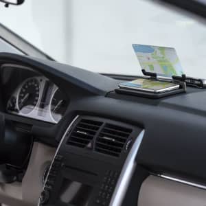 A car dashboard featuring the Wantol Dashboard Holder, displaying a phone with a map on a black surface.