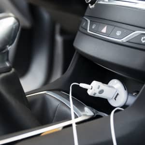 A white Bluetooth receiver is plugged into a car's console, with a cable connected, amidst black interior features.
