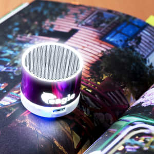 A compact purple speaker with an illuminated base, placed on a magazine showcasing vibrant images.