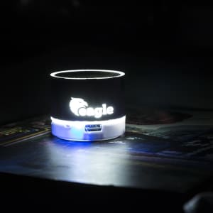 A compact black and white speaker with a lighted base, featuring a logo.