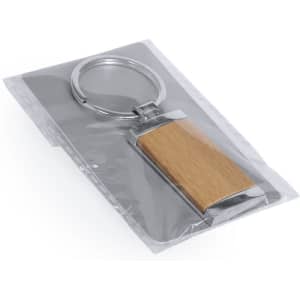 A wooden keyring with a metallic frame, packaged in a transparent pouch.