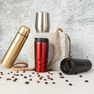 A collection of insulated travel mugs and cups in gold, silver, and red, arranged on a textured surface with coffee beans scattered around.