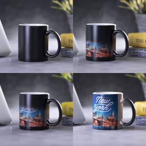 A coffee mug featuring a black exterior with a New York design on the white interior. It has a handle and a logo.