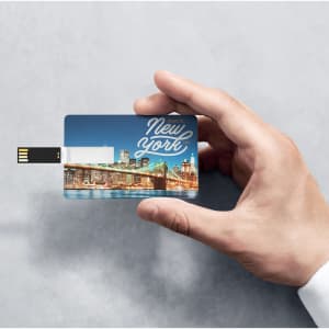 A hand holding a blue and white USB memory stick featuring a New York cityscape design.