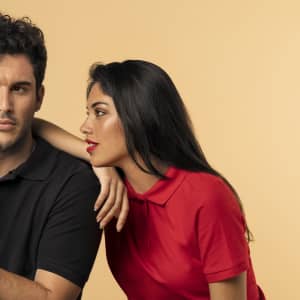 A woman in a red polo shirt leans towards a man in a black polo shirt against a neutral background.