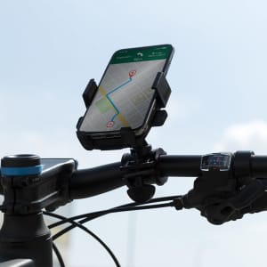 A black phone holder mounted on a bicycle handlebar, displaying a map on the phone screen against a bright sky.