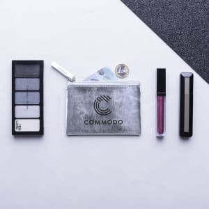 A silver pouch with a logo, surrounded by cosmetics including eyeshadow and lip gloss.