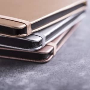 A stack of Bodley Notepads in gold, silver, and rose gold shades, featuring sleek covers and a branding logo.