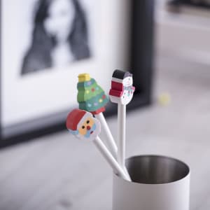 Three festive pencils with colourful toppers: Santa, a Christmas tree, and a snowman, in a metal holder.