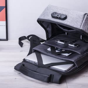 A grey anti-theft backpack with compartments for a laptop, pens, and a phone, featuring a secure closure mechanism.