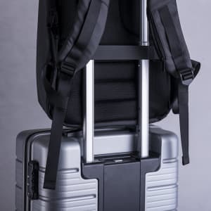 A black anti-theft backpack is shown secured on a silver suitcase, featuring adjustable straps and a sleek design.