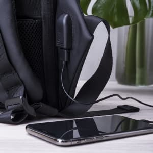 A black anti-theft backpack with a charging port, next to a smartphone on a surface.