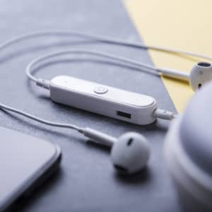 White Sopral earphones resting on a grey surface, featuring a control module and connected to a device.