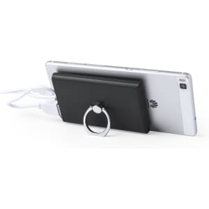 A black power bank is connected to a smartphone, featuring a ring holder for support.