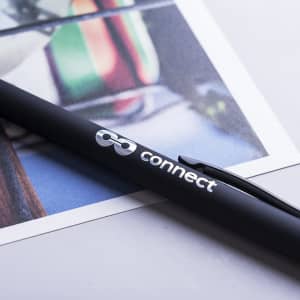 A black stylus touch ball pen with a clip, featuring a logo, resting on a printed image.