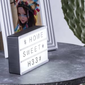 A light box in grey and white, featuring interchangeable letters, displayed on a table alongside a framed photo.