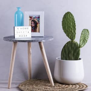 A light box, blue vase, framed photo, and a cactus sit on a round grey table with wooden legs.