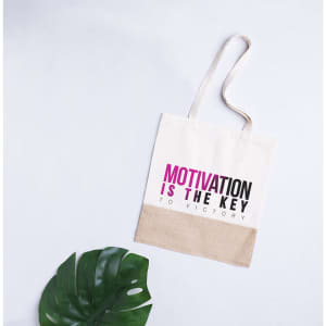 A cream tote bag with a pink and black printed slogan, featuring a brown bottom section and a logo.
