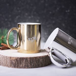 A drink mug set featuring a shiny gold and a sleek silver mug, placed on a wooden slice with festive decorations.