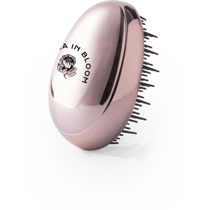 A rose gold hairbrush with bristles, featuring a floral logo on the handle.