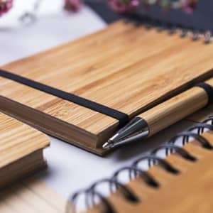 A bamboo notebook with a black elastic band, accompanied by a bamboo pen and spiral-bound notebooks.