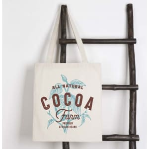 A natural-coloured tote bag featuring a design with cocoa plants and branding, hanging on a wooden rack.