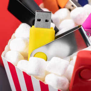 A group of colourful USB flash drives, including yellow and red, placed among white packing peanuts in a popcorn-style container.