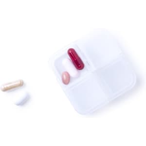 A white pillbox with four compartments, containing a red capsule, a pink tablet, and other pills beside it.