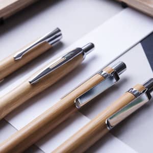 A collection of wooden pens in natural wood tones with silver metal accents, arranged on a flat surface.