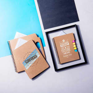A set of two spiral-bound notebooks with a kraft paper cover, featuring a logo and colourful sticky tabs.