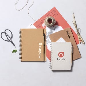 Two spiral-bound notebooks in brown and grey, accompanied by scissors, string, and decorative paper elements.