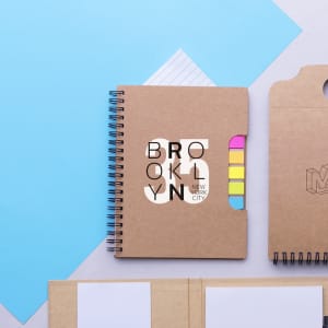 A notepad with a brown cover, spiral binding, and coloured tabs on the side, surrounded by blue sheets of paper.