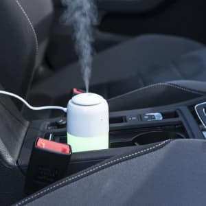 A small grey and green humidifier sits in a car’s cup holder, emitting a stream of mist.