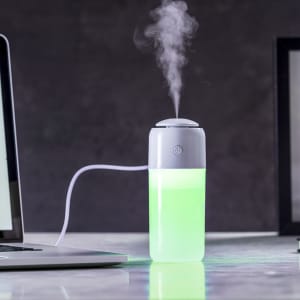 A humidifier in a sleek design with a grey top and glowing green base, emitting a gentle mist.