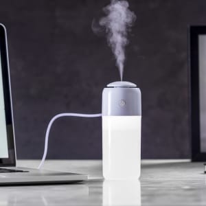 A humidifier in grey and white emits steam, placed next to a laptop on a marble surface.