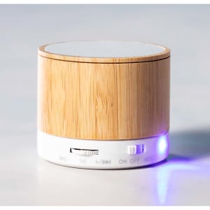 A bamboo Bluetooth speaker with a white base and control buttons, featuring a small blue indicator light.