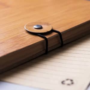A bamboo notebook featuring a round closure and black elastic. The pages are lined and tan in colour.