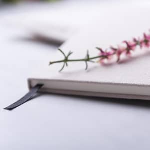 A notepad with a cream cover and a black ribbon bookmark, adorned with a small pink flower sprig.